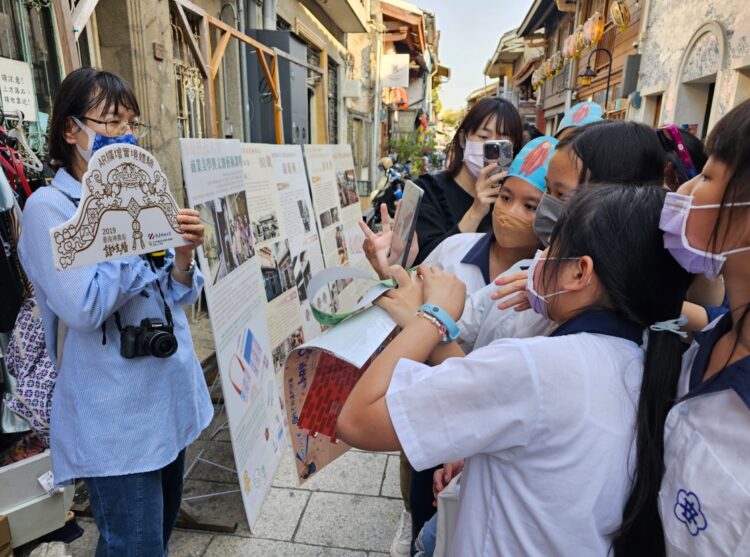 ▲學童體驗南臺科大計畫團隊透過AR技術讓神農街口裝置藝術鐵支牆裡使用的神農街元素舞動認識創作意象。（圖／南臺科大提供）